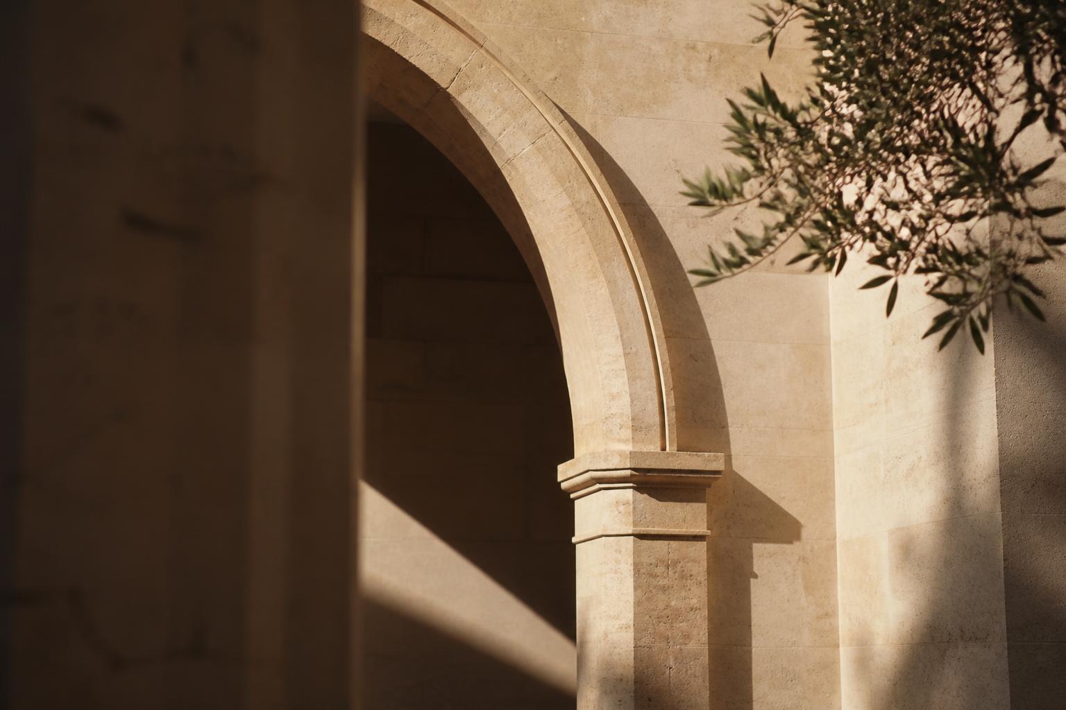 Sunlight falling across a pale stone arch with an olive branch overhead